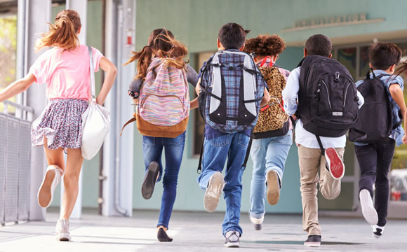 niños de espaldas con mochilas corriendo