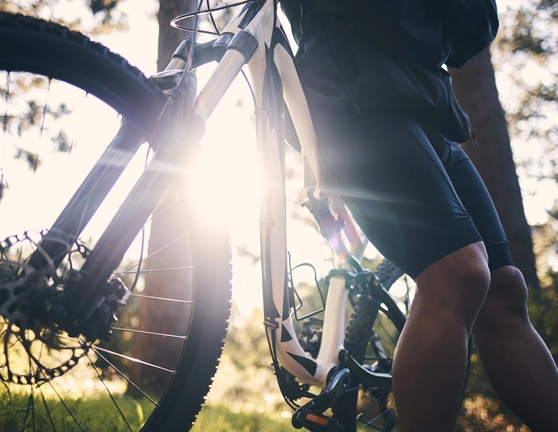 Persona apoyada en una bicicleta mientras una ruta con el sol de fondo
